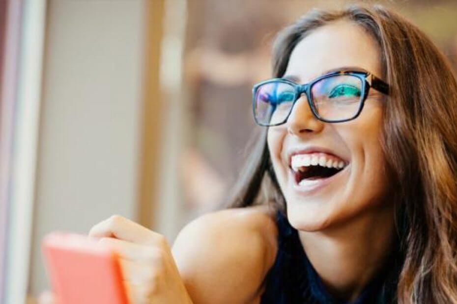 mulher de oculos rindo com um celular na mao